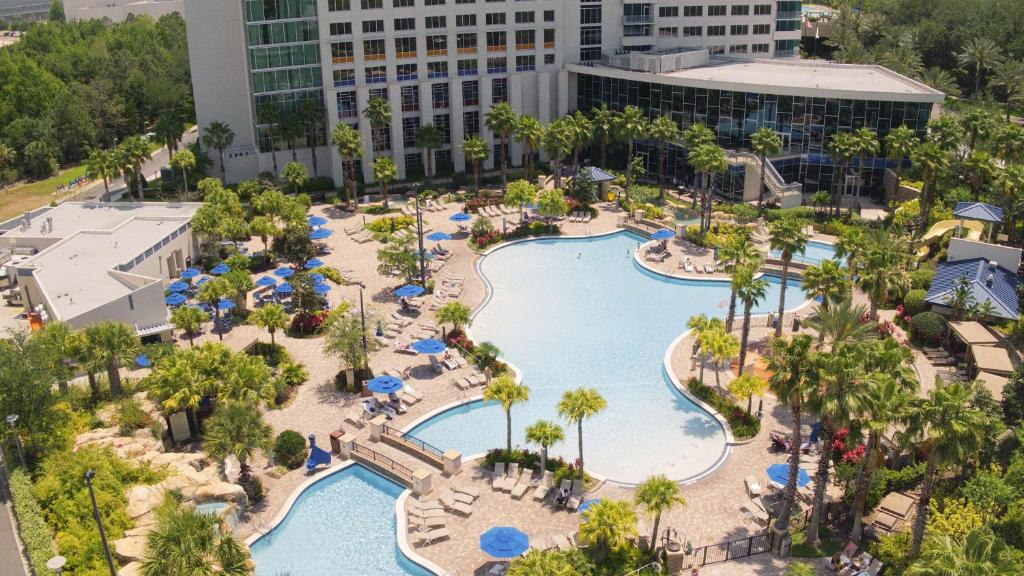 vista de cima do Hyatt Regency Orlando com uma piscina enorme, ponte ligando os dois lados, com árvores e o prédio do hotel mais ao fundo, para ilustrar o post sobre hotéis em Orlando