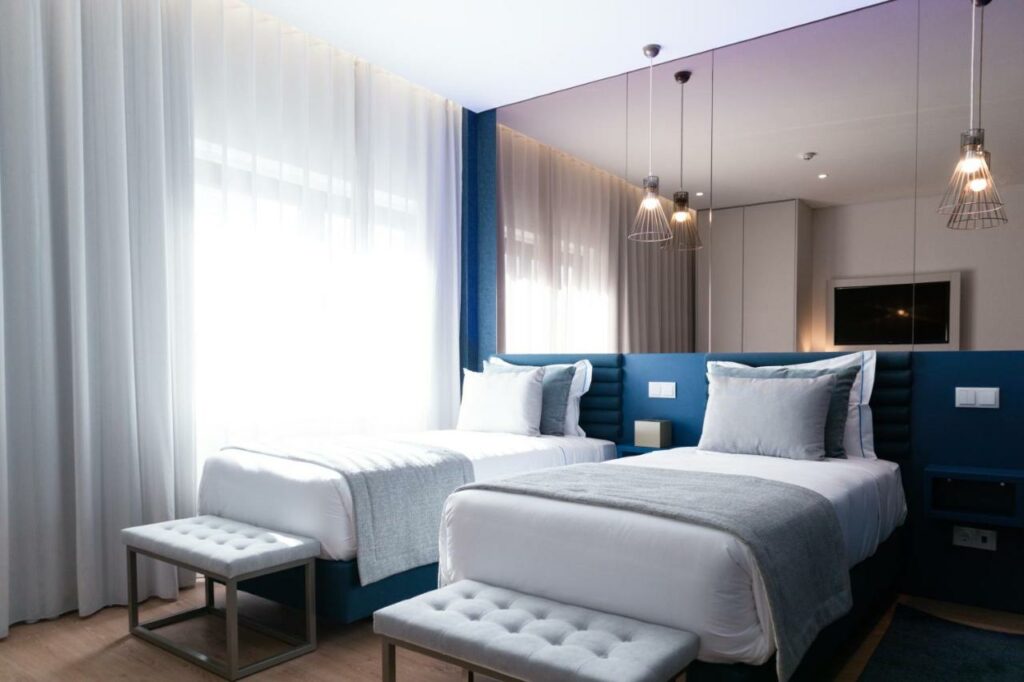 Quarto no Zurin Charm Hotel, com duas camas de solteiro, recamier nos pés, amplo espelho atrás da cabeceira, e cortina voil