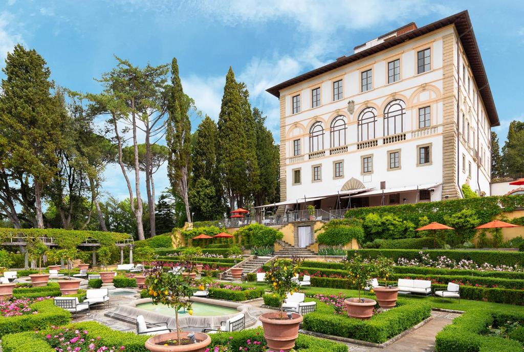 Jardim amplo na entrada do Il Salviatino, um dos hotéis na Toscana, com flores coloridas, vasos de barro, gramado verde e prédio clássico da propriedade