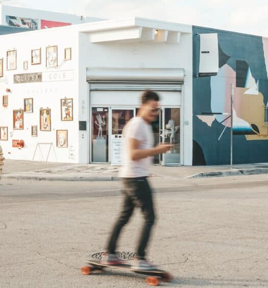 pessoa andando de skate enquanto mexe no celular com paredes grafitadas e coloridas de fundo em Wynwood que pode ser fotografado com o chip celular Miami