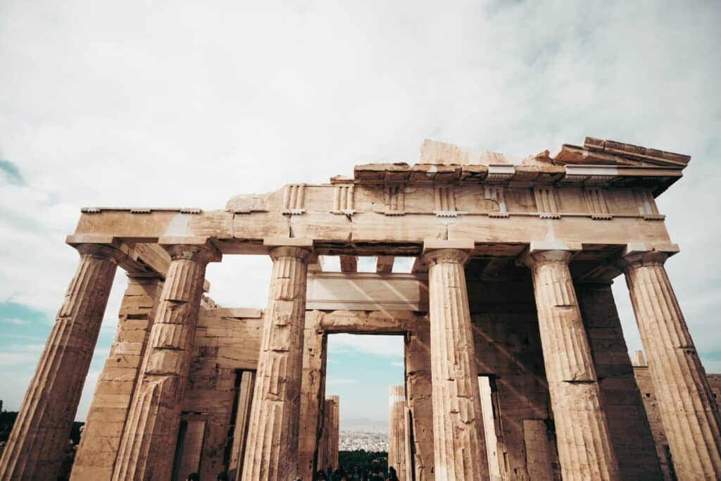 vista de frente de um monumento mais ou menos em ruínas, principalmente a parte do topo que falta um pedaço, a estrutura possui diversas colunas, na Acrópole de Atenas, que ilustra o post de chip celular Grécia