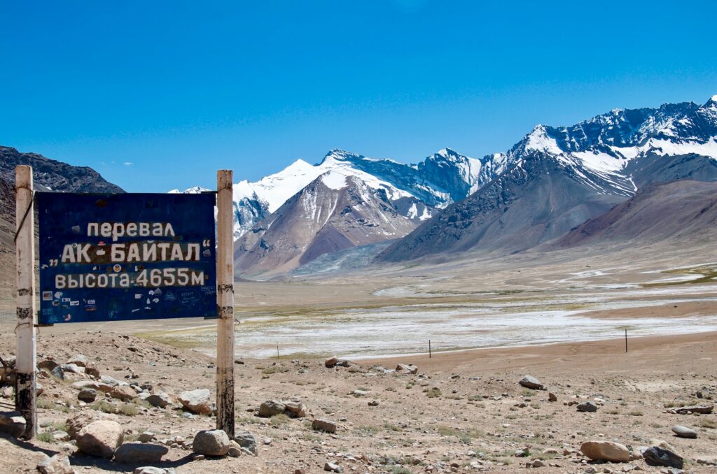 Placa de sinalização de madeira perto de campo marrom e montanha durante o dia, ilustrando post seguro viagem Tajiquistão.