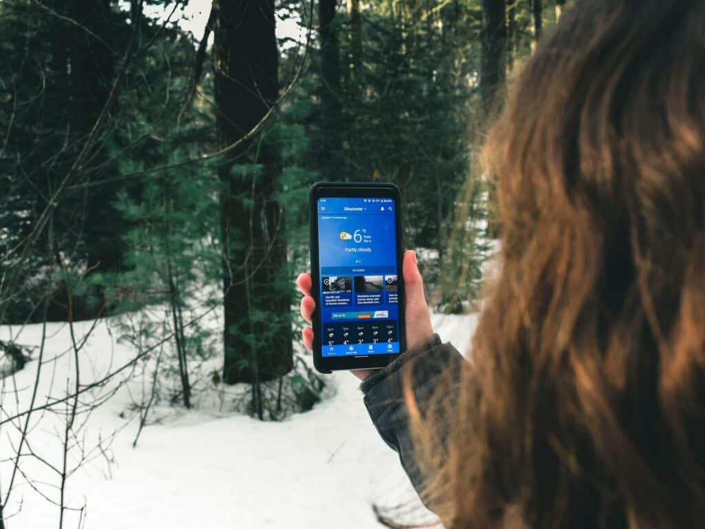 Uma moça segurando um celular e, ao redor, há muita neve e algumas árvores, para representar chip celular América do Norte