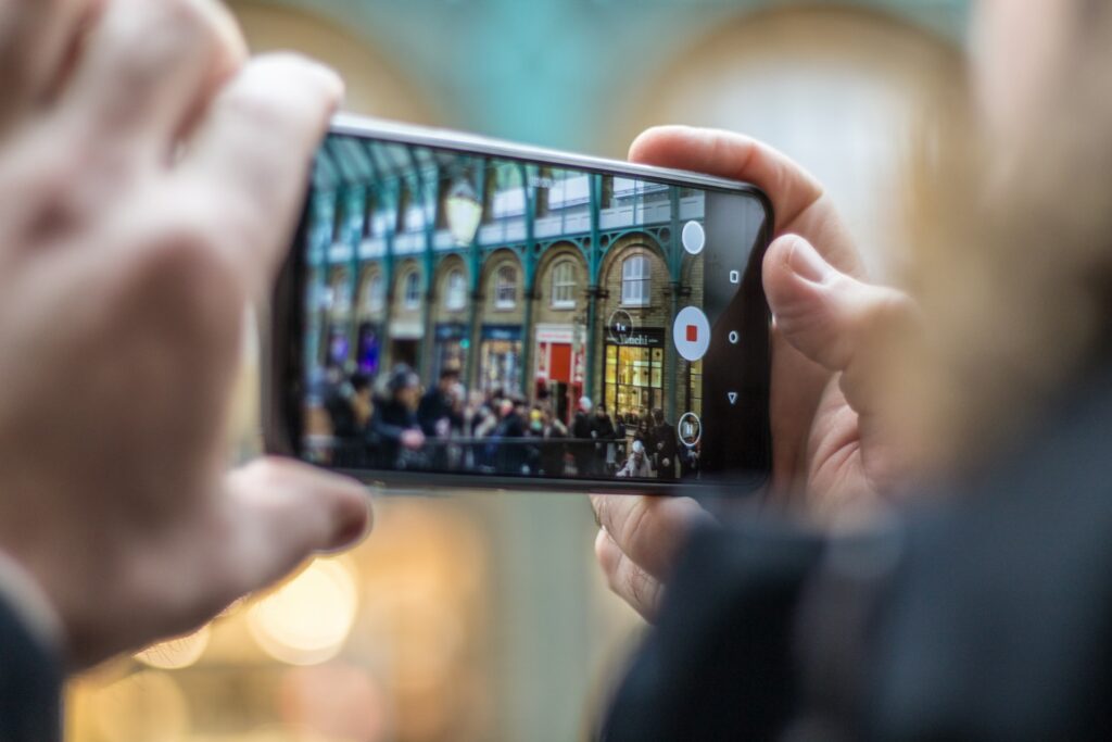 Mãos masculinas brancas segurando um celular na horizontal enquanto fotografa algumas lojas na Convent Garden em Londres