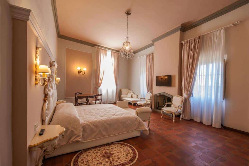 Quarto do Art Hotel Villa Agape, um dos hotéis em Florença, de 30 m², com cama de casal, mesa redonda com duas cadeiras, sofá e duas cadeiras estofadas de época, lustre suspenso e janelas com cortinas altas enfeitando o espaço