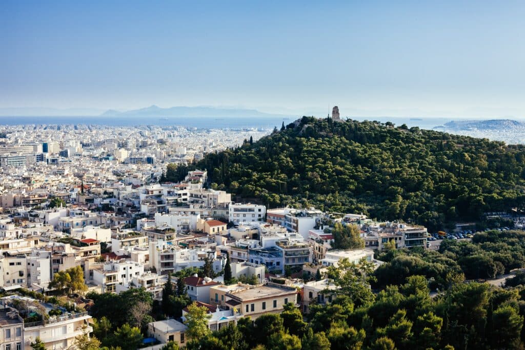 Vista da cidade de Atenas cheia de casas, mar ao fundo e céu claro.