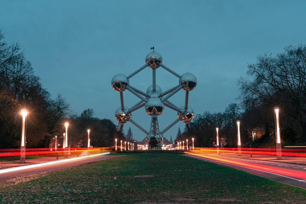 vista à noite do monumento Atomium, em Bruxelas, que emula o formato de um átomo (bolas prateadas ligadas entre si formando formas geométricas), com luzes de carro passando rápido de ambos os lados