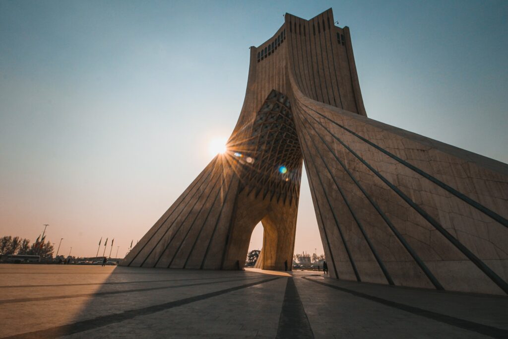Estrutura de concreto marrom em formato de V ao contrário com o sol brilhando atrás para ilustrar o post seguro viagem Irã. - Foto: Alireza Heydarifard via Unsplash