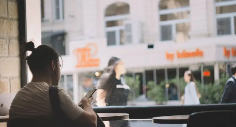 Rapaz com celular na mão sentado em uma mesa com mochila a frente em Azerbaijão.
