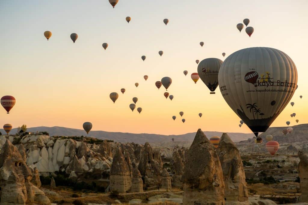 Vários balões sobrevoando formações rochosas ao nascer do sol. - Foto: Dana Andreea Gheorghe via Unsplash