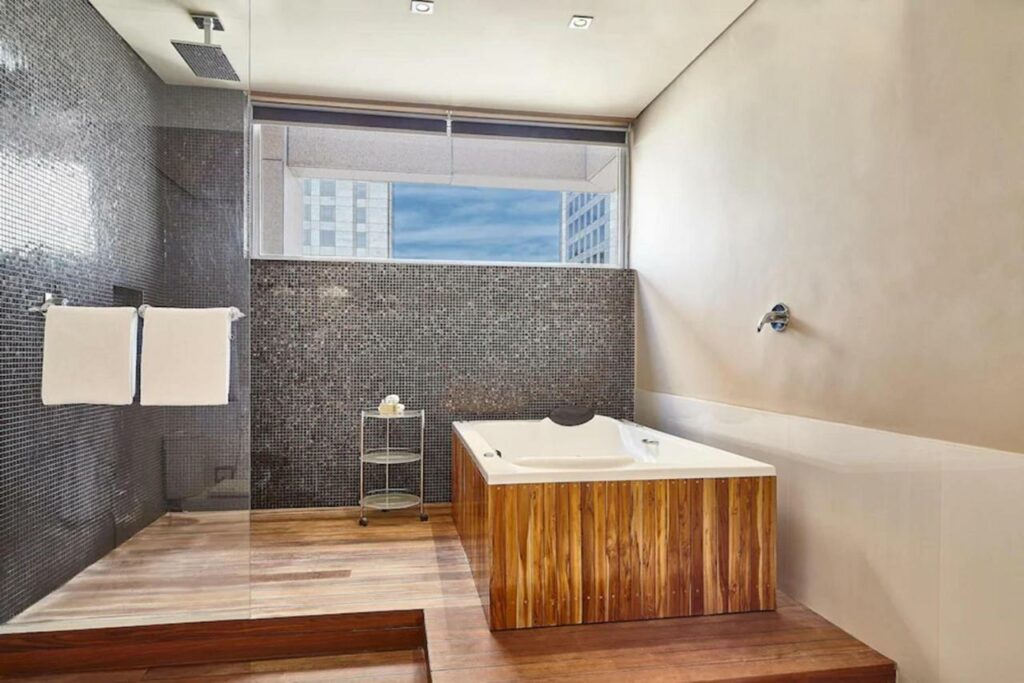 Banheiro amplo do Sheraton São Paulo WTC Hotel com uma janela mais alta, um box grande com uma banheira disponível e um pequeno deck ao redor, para representar hotéis perto do Autódromo de Interlagos