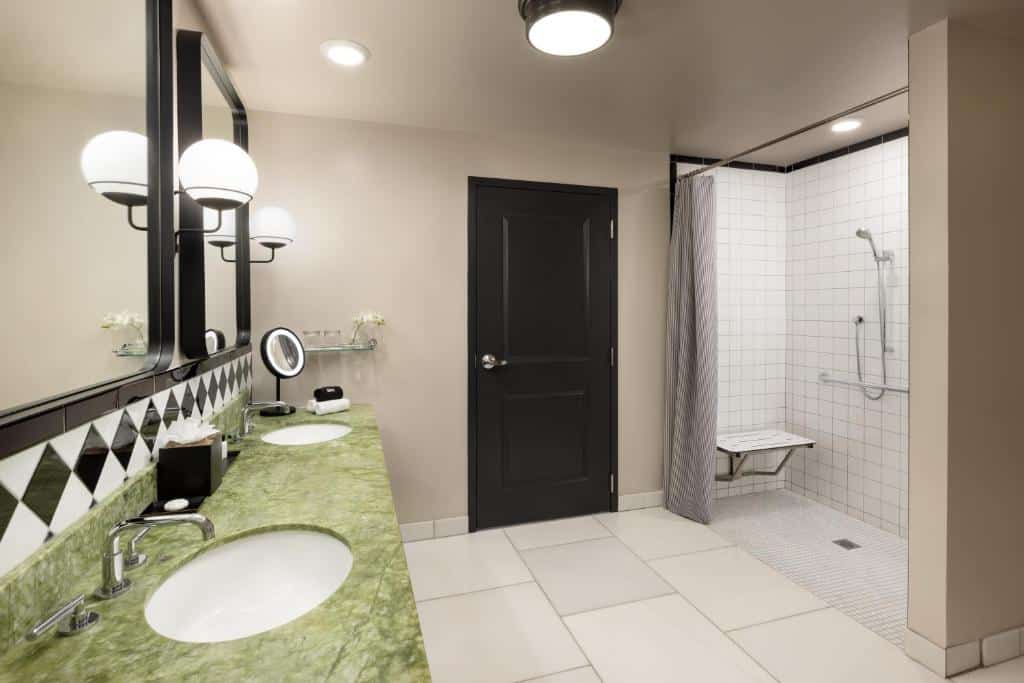 Banheiro do The Candler Hotel Atlanta, Curio Collection by Hilton com espaço, pia baixa, chuveiro com barra de segurança.