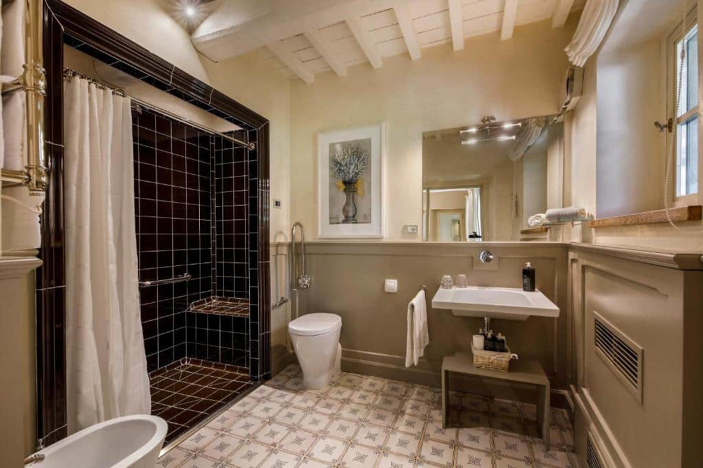 Banheiro do quarto duplo do Borgo Del Cabreo, um dos hotéis na Toscana, com vaso sanitário, bidê, pia, bastante espaço entre os objetivos e área separada para banho com barra de apoio e assento para cadeirantes