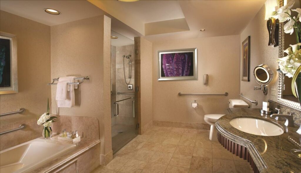 Banheiro adaptado do Bellagio com barras de apoio na área da privada, box, pia e banheira, a pia é mais baixa e o local é bem espaçoso