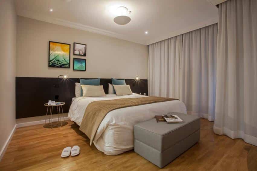 Quarto do Blue Tree Premium Morumbi com uma cama de casal com almofadas, chão de madeira, uma janela com cortinas e luminárias de parede perto da cama, para representar hotéis para o The Town em SP