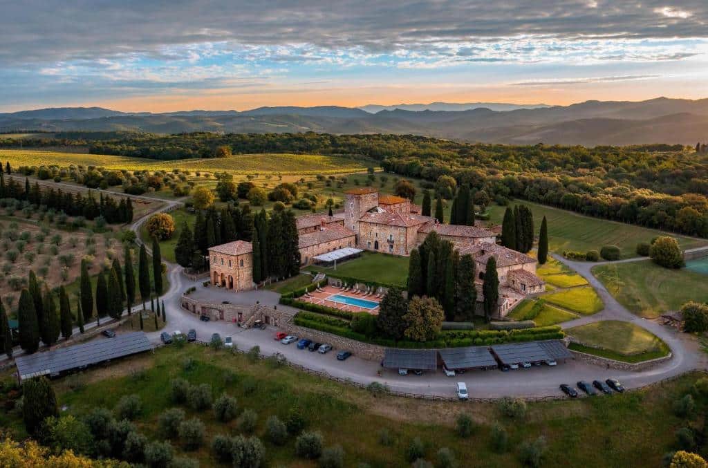 Vista aérea do Borgo Scopeto Wine & Country Relais, localizado numa área cheia de verde, com diversas árvores e gramado verde em volta, e prédios do local (parecendo um castelo), com paredes de tijolinhos e piscina