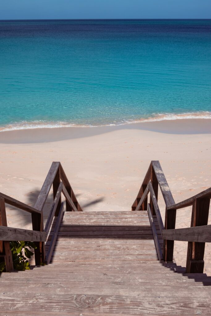 Escada de madeira em direção a uma praia de águas turquesas. - Foto: Shaquille Campbell via Unsplash