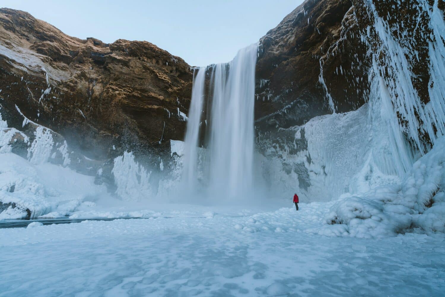 pessoa de costas observando uma cachoeira bem alta, a Skógafoss, com muita neve em volta e uma grande parede de pedra, para ilustrar o post de chip celular Islândia