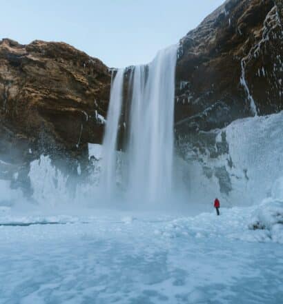 pessoa de costas observando uma cachoeira bem alta, a Skógafoss, com muita neve em volta e uma grande parede de pedra, para ilustrar o post de chip celular Islândia