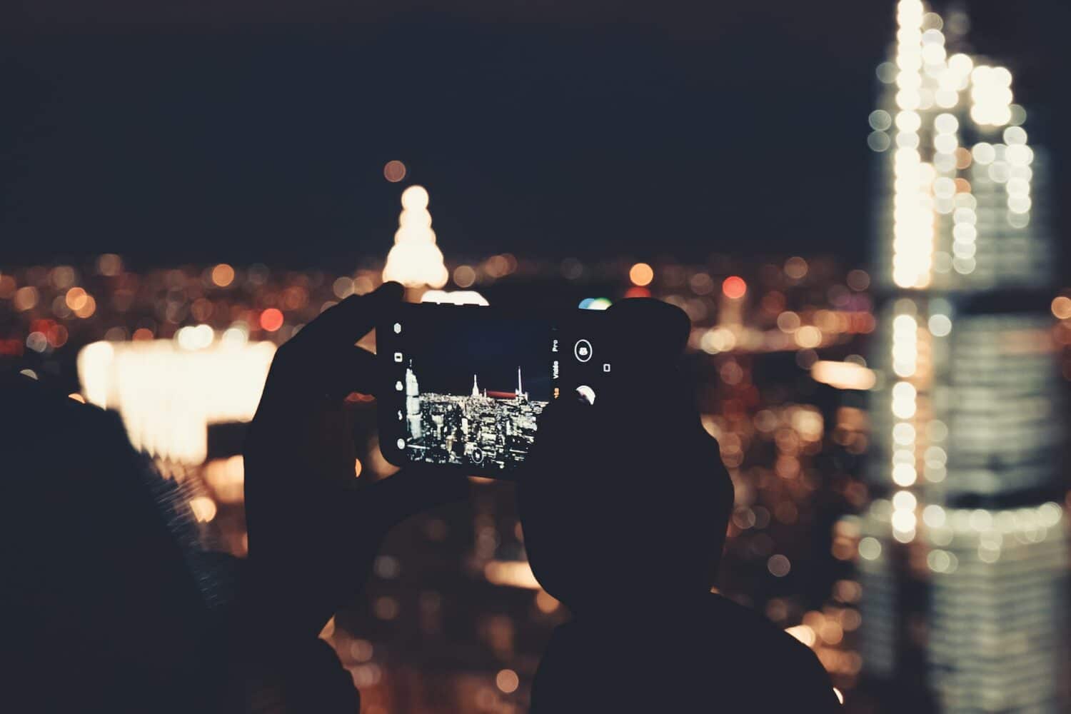Uma pessoa segurando um celular para tirar uma foto de um prédio iluminado em Nova York