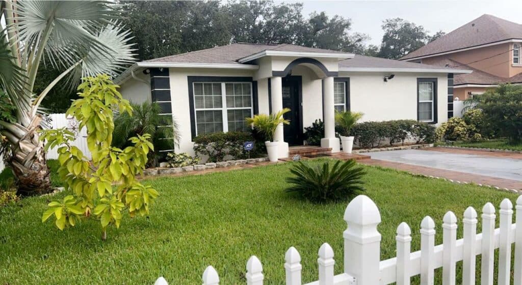 Entrada da Caribbean Splendor Vacation Rental near Bush Gardens Tampa FL, uma casa branca com detalhes em cinza e um amplo gramado na frente