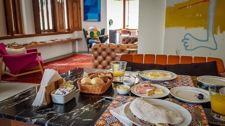 Mesa de café da manhã da Casa Marques. Há suco de laranja, tapioca, frios, pães e ovos fritos.