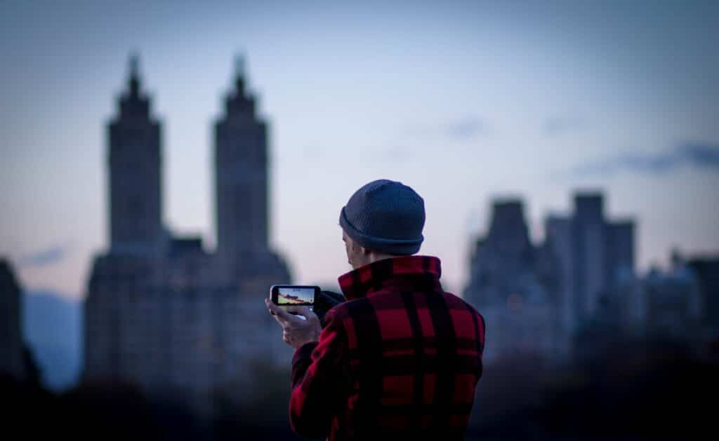 Homem com blusa listrada vermelha segurando celular e fotografando a região de Central Park, em Nova York