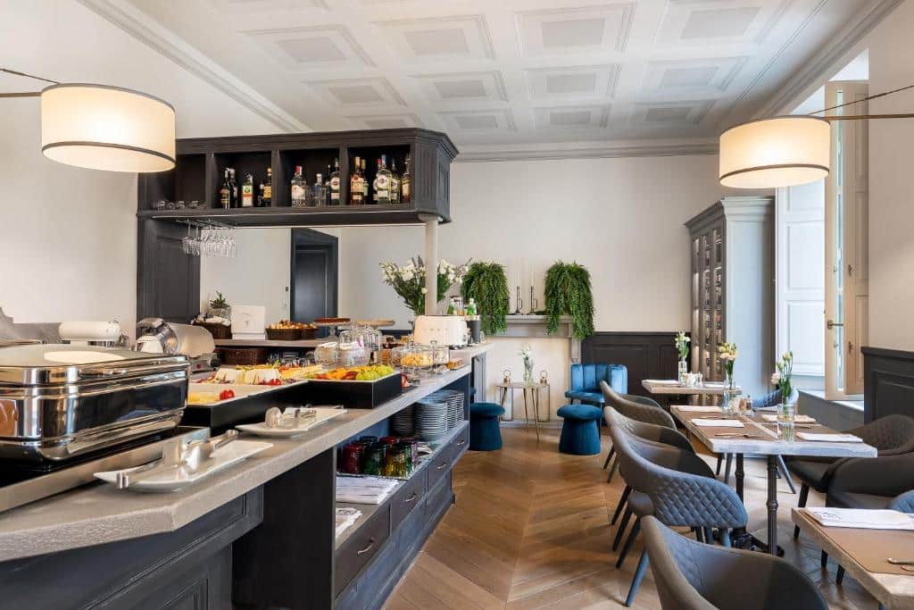 Área de refeição do Corte Calzaiuoli Elegant Suites, um dos hotéis em Florença, com balcão com comidas, pequena adega com garrafas de bebidas alcoólicas, e mesas ao lado com cadeiras estofadas cinza