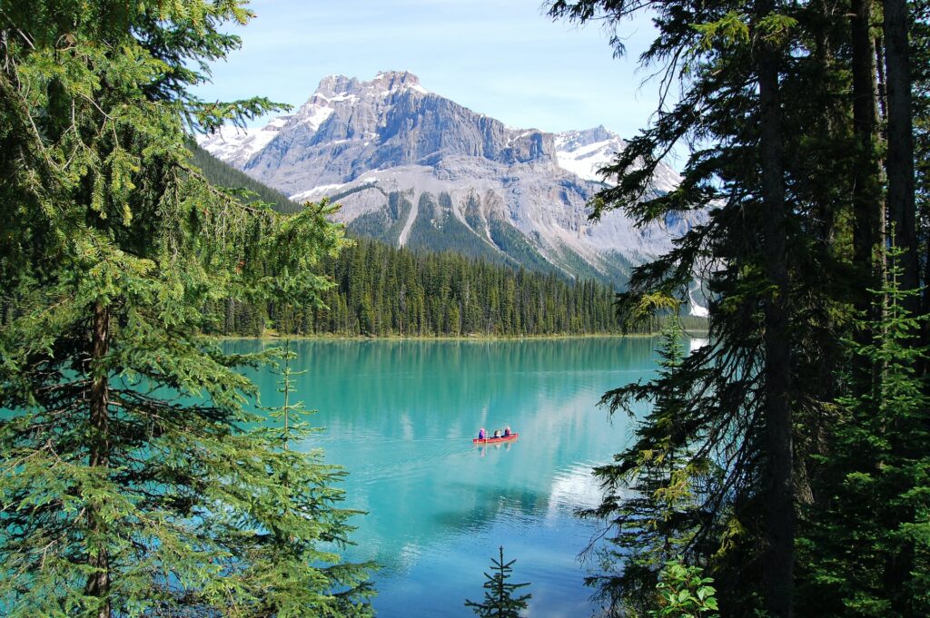 Emerald Lake com águas nos tons de azul e verde, árvores em volta e um barco vermelho ao centro, durante o dia.