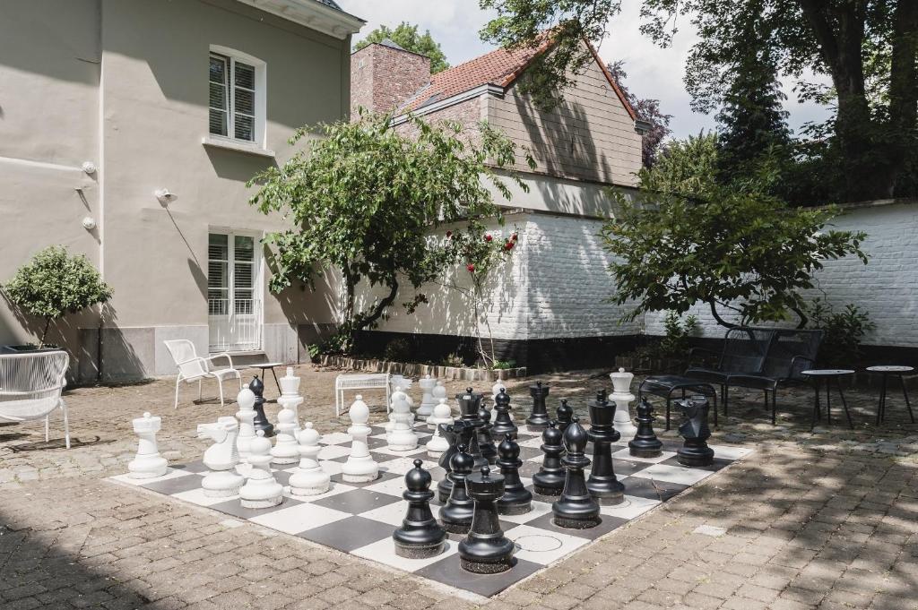 área externa do Hotel Made In Louise, um dos hotéis em Bruxelas, com árvores e piso de pedra com cadeiras brancas e um jogo com peças gigante de xadrez no chão
