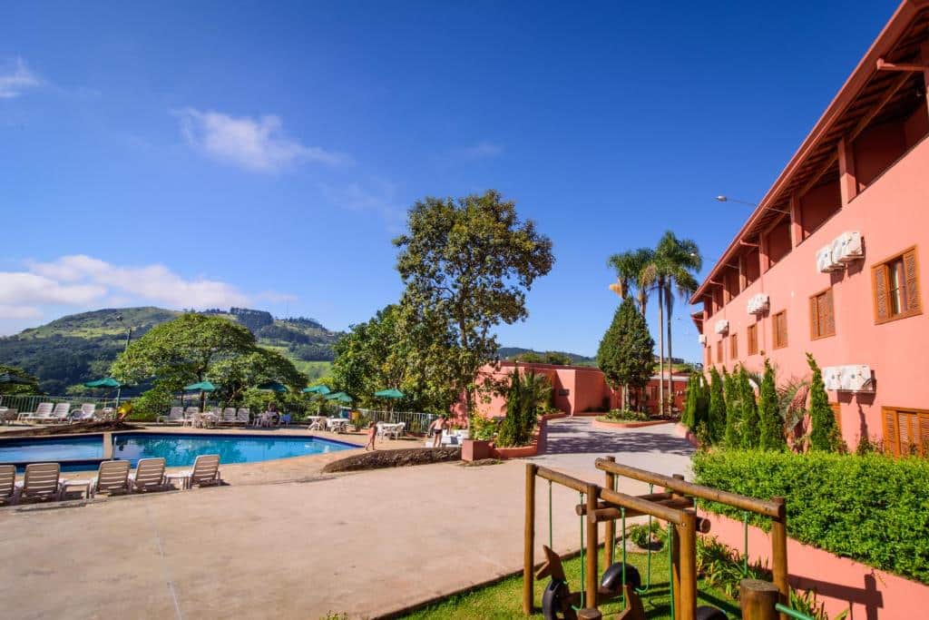 piscina com vista para as montanhas e estrutura do hotel ao lado em três andares em tons laranja com espaço amplo e detalhes em madeiras no Hotel Refúgio Vista Serrana em Mairiporã