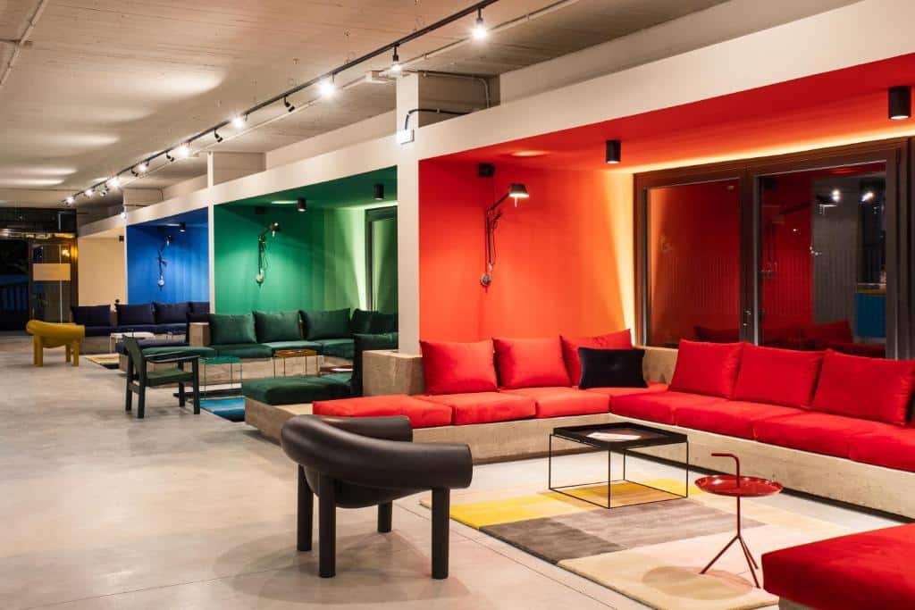 áreas decoradas do Ibis Styles Roma Aurelia com poltrona e sofá quadrados com cada um desses ambientes de uma cor do arco-íris, vermelho, verde, azul, amarelo... sendo um dos hotéis Ibis em Roma