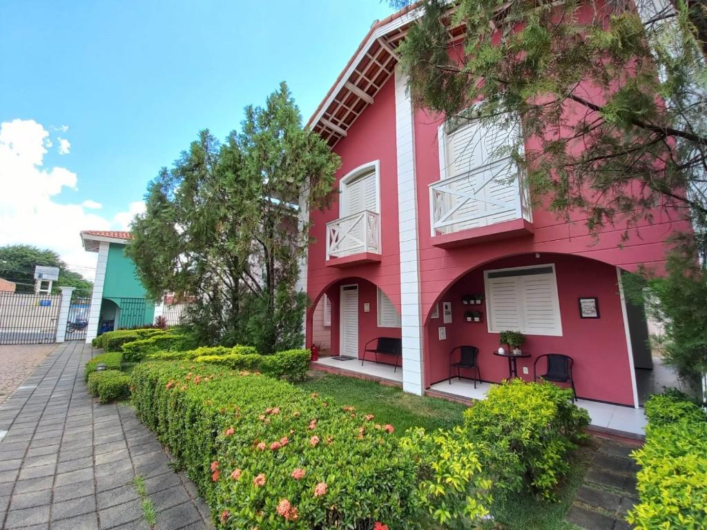 fachada vermelha com muro de grama com flores e mesinha na varanda na Casa condomínio 2 suítes em Juazeiro do Norte