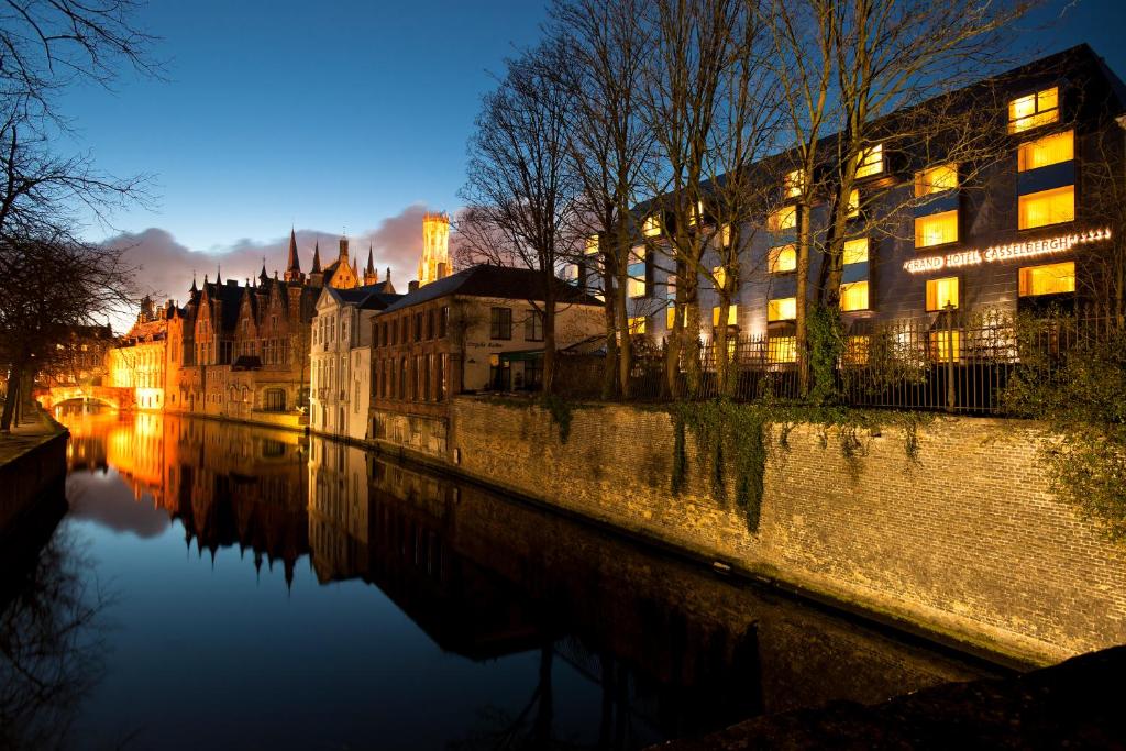 vista da fachada do Grand Hotel Casselbergh Brugge, um dos hotéis em Bruges, na beira do rio, com algumas árvores na frente e outras construções