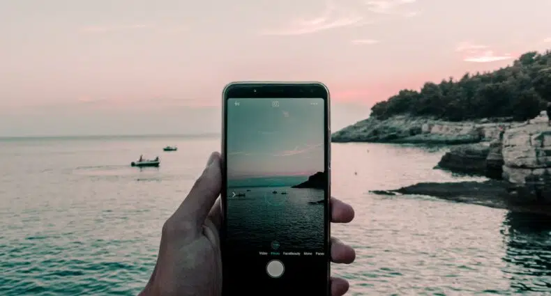 Mão segurando um celular preto, com a tela da câmera aberta mostrando a imagem de uma praia localizada na Croácia
