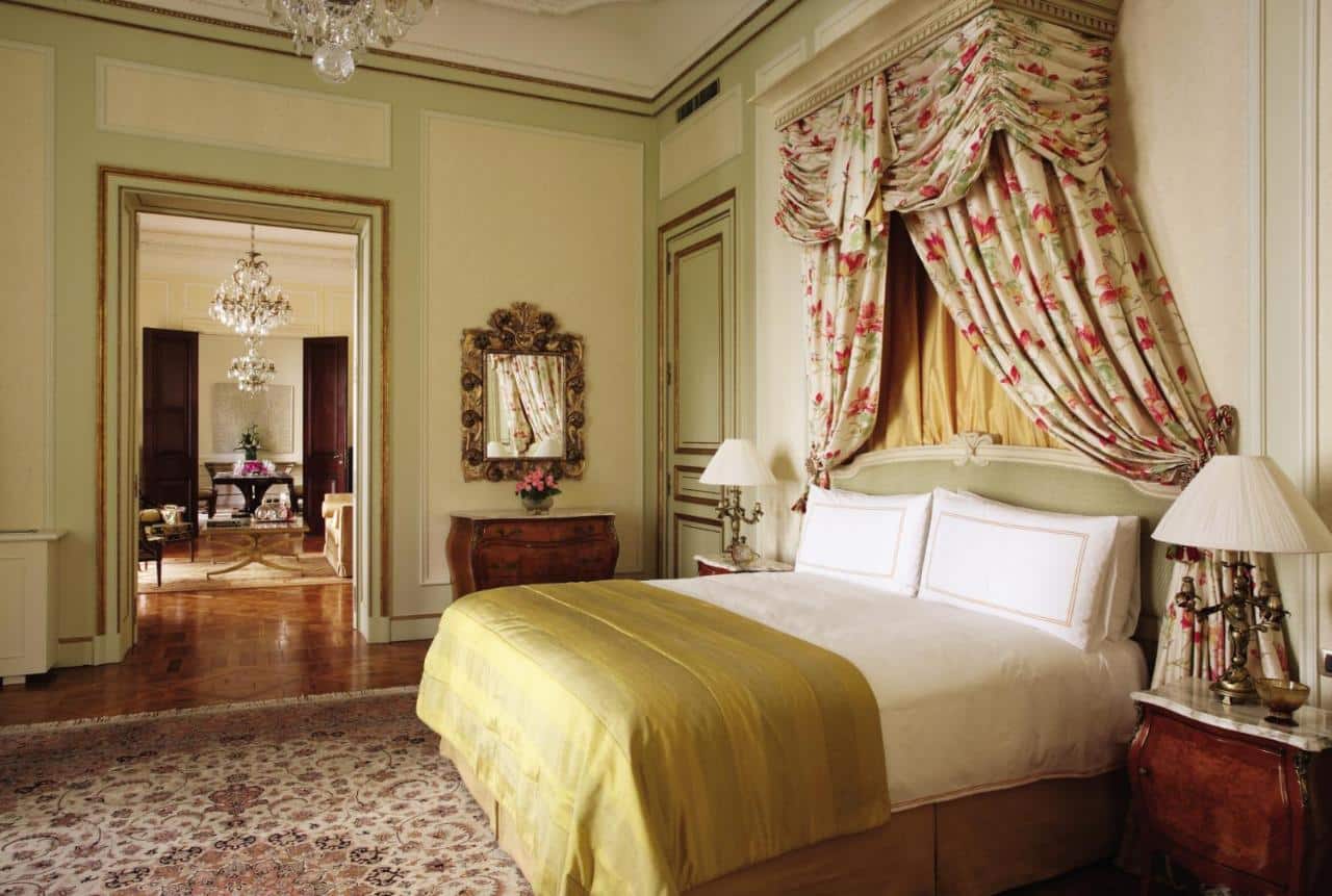 Um quarto no Four Seasons Hotel Buenos Aires todo em estilo renascentista, com uma cama de casal, um tapete persa, um espelho, uma cômoda de madeira e um lustre
