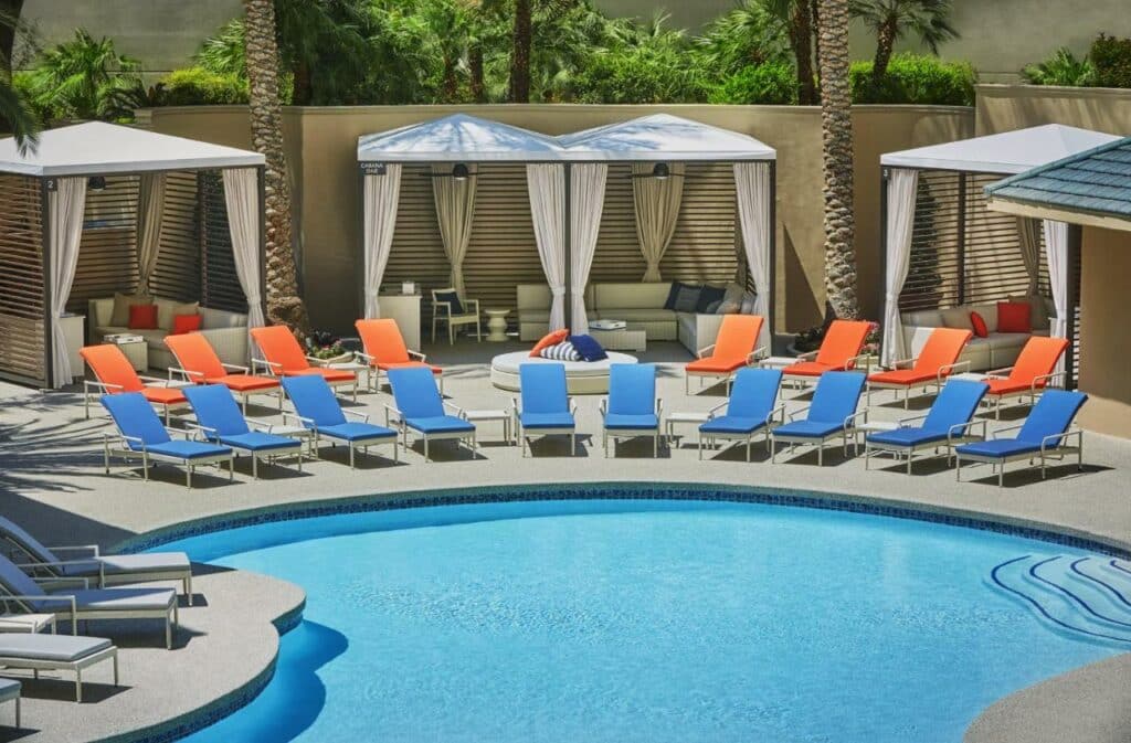 Piscina do Four Seasons Hotel Las Vegas com um deck repleto de espreguiçadeiras azuis e laranjas, além de alguns bangalôs com sofás mais ao fundo