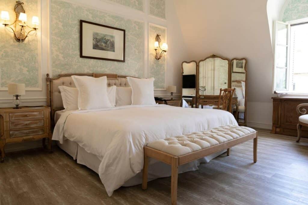Quarto amplo no Four Seasons Hotel Buenos Aires com uma cama de casal, duas mesinhas de cabeceira com abajur em cima deles, um chão de madeira, uma parede atrás da cama com papel de parede verde e branco, um espelho do lado direito do quarto, e uma janela