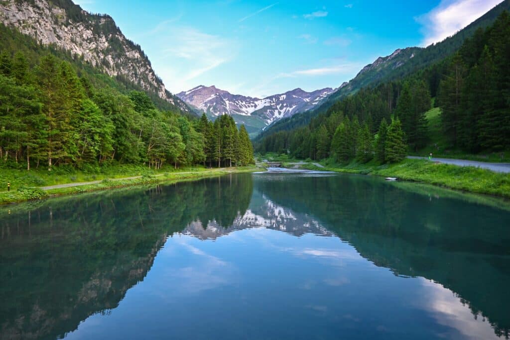 Árvores esverdeadas ao redor de um lago para ilustrar o post de chip de celular para Liechtenstein. Ao fundo podemos ver montanhas com gelo. - Foto: Ondrej Bocek via Unsplash