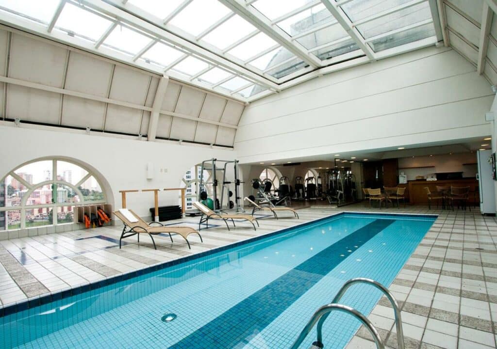 Uma piscina coberta no Gran Estanplaza Berrini com teto de vidro com um deck ao redor com espreguiçadeiras