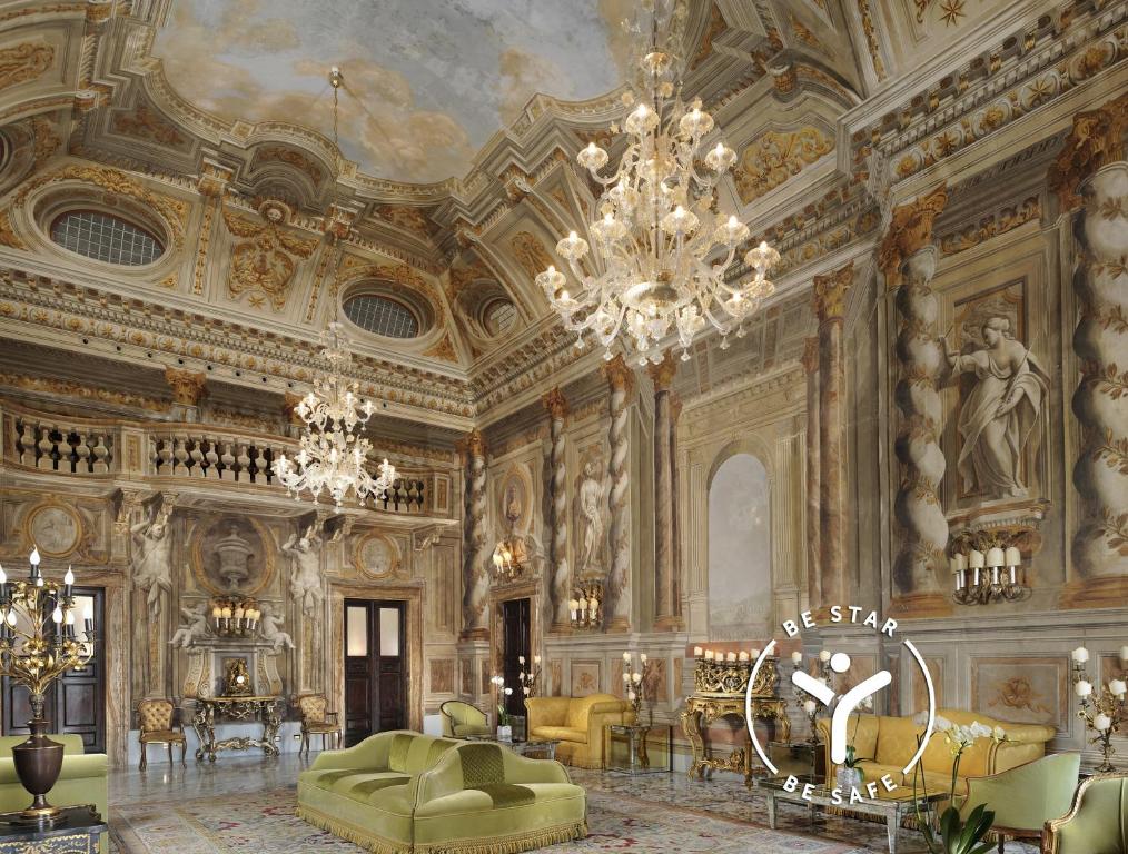Interior do Grand Hotel Continental Siena, um dos hotéis na Toscana, com uma aparência similar a um castelo, com pinturas nas paredes, lustres grandes e pinturas no teto, além de sofás e móveis de época