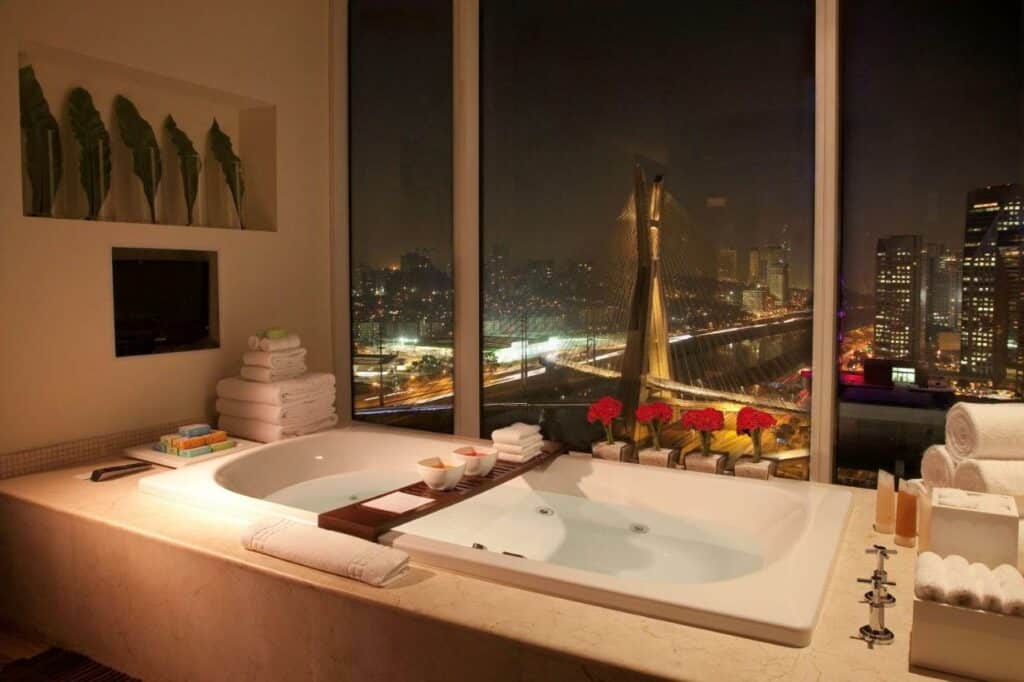 Banheiro no Grand Hyatt São Paulo com uma banheira com uma janela gigante com vista para a ponte estaiada, ao redor da banheira há diversas toalhas e sabonetes