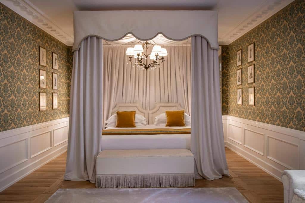 Quarto do Helvetia&Bristol Firenze, com 38 m², uma cama branca com lustre iluminando em cima, além de paredes decoradas com papel de parede e quadros