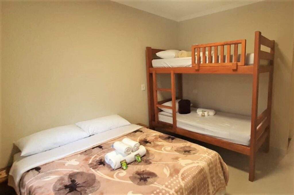 Quarto no Hostel B2B SP com uma beliche de madeira com toalhas e travesseiros, além de uma cama de casal com toalhas também sob a cama
