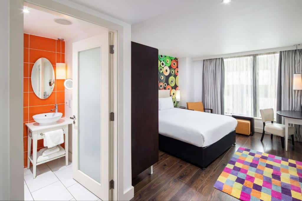 Quarto individual do Hotel Indigo Liverpool, com cama de solteiro, tapete colorido e banheiro com azulejos laranja e pia branca