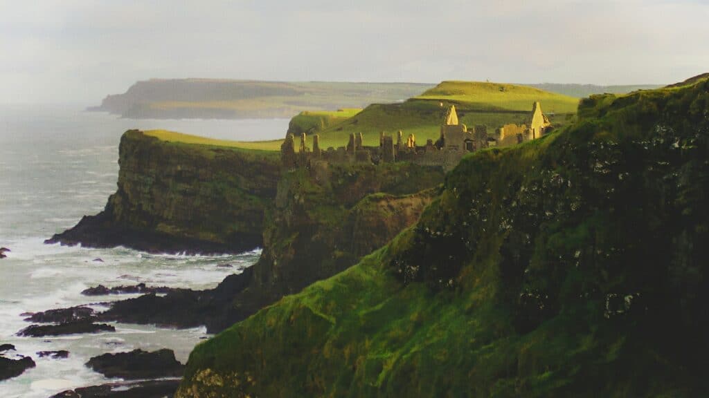 Ruína do Castelo de Dunluce, Irlanda do Norte em cima de uma montanha com gramas verde, céu azul e em volta da montanha o mar. Representa chip celular Irlanda do Norte