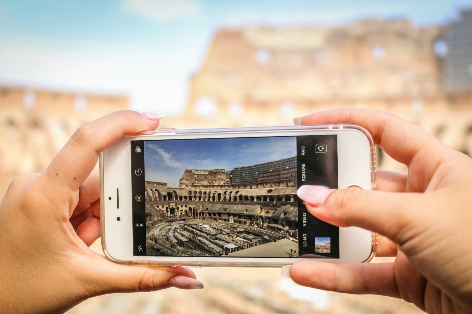 Uma moça segurando um celular na horizontal enquanto fotografa um dos monumentos históricos de Roma com um celular branco