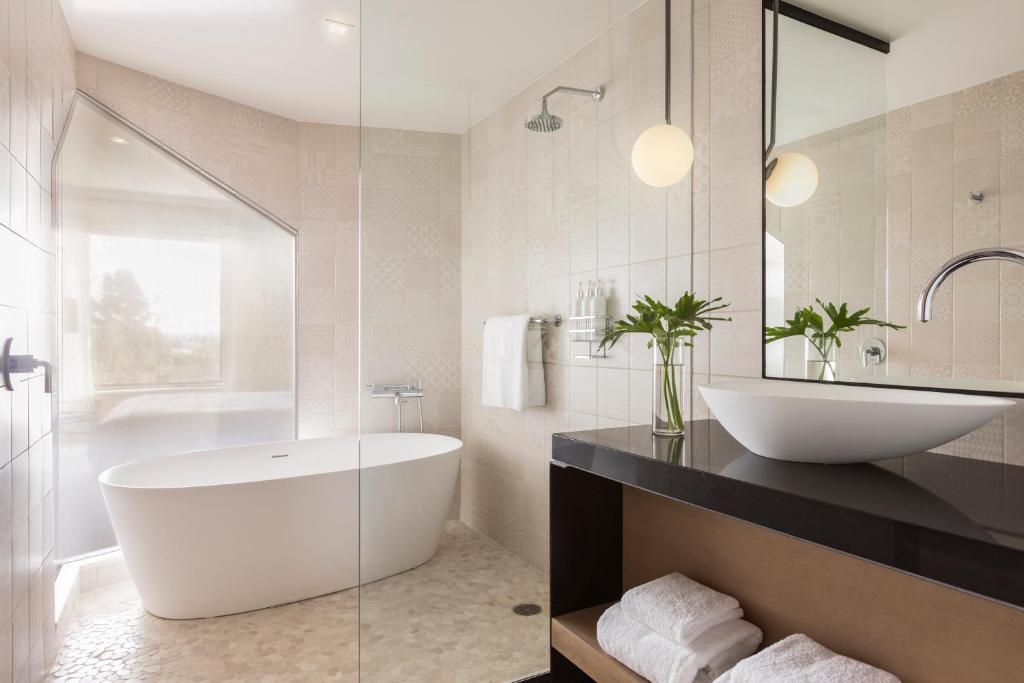 Banheiro no Kimpton La Peer Hotel, an IHG Hotel com uma banheira oval dentro de um box bem amplo, do lado direito há uma pia ampla com prateleiras embaixo com toalhas brancas dobradas