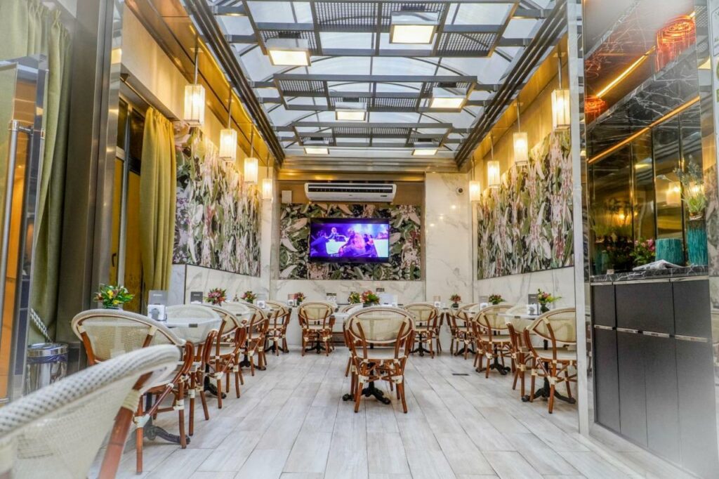 Salão do restaurante do Konke Buenos Aires Hotel com chão de madeira, mesas redondas com cadeiras de madeira, há uma ampla televisão e um ar-condicionado logo acima, o teto tem partes de vidro que iluminam o local
