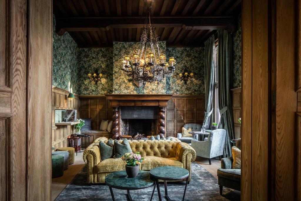área de lareira decorada de forma luxuosa do Hotel De Orangerie, um dos hotéis em Bruges, com lustre e detalhes em verde escuro e sofá claro e papel de parede trabalhado